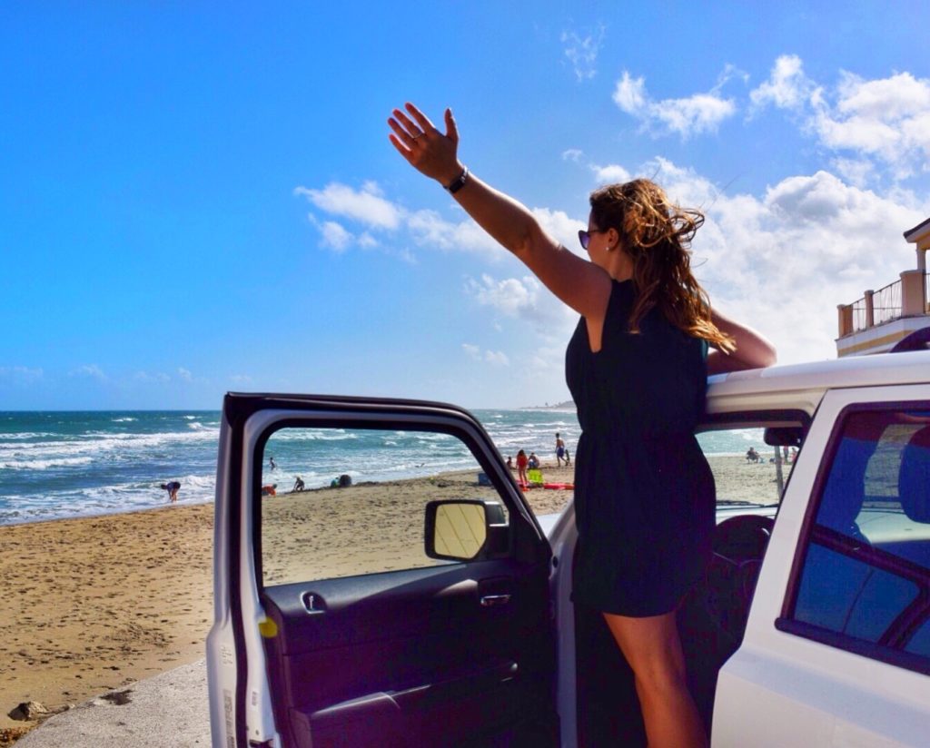 woman standing in her car by the beach